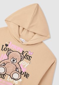 Felpa beige con una morbida grafica di orso testurizzata, testo rosa e nero, e un accento di farfalla. Presenta un classico design con cappuccio.