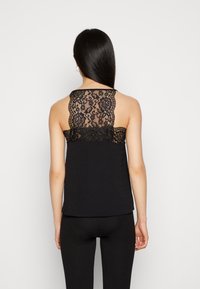 Débardeur noir avec un dos en dentelle à motif floral et bords festonnés, tissu lisse et coupe décontractée.