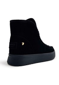 Botines de ante negro con una superficie texturada, una suela gruesa y cordones decorativos. Presentan un pequeño logo en el lateral y un talón acolchado.