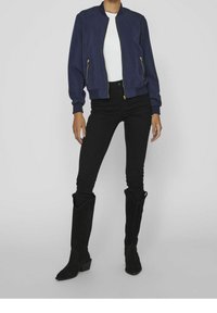 Marinblå bomberjacka med guldfärgade blixtlåsdetaljer, vit t-shirt, svarta skinny jeans och svarta knähöga mockastövlar med klack.