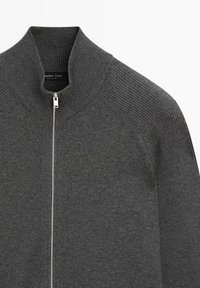 Cardigan grigio con zip e collo alto, texture a coste sulle spalle e tessuto liscio sul corpo. La zip è color argento.