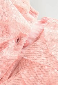 Close-up of pink mesh fabric with polka dots, ruffled edges, and matching pink buttons on a garment.