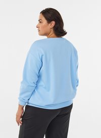 Light blue sweatshirt in soft fabric, featuring a wide neckline and long sleeves. Worn with black pants, showing a relaxed fit.