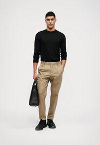 Juodas ilgas rankovės marškinėlis, smėlio spalvos raukšlės kelnės, juodi sportbačiai ir juoda kuprinė. Paprastas, pritaikytas dizainas su prigludusia siluetu.