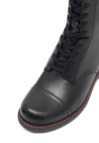 Černá kožená bota s kulatou špičkou, s hladkým povrchem, červeným švem po celé délce podrážky a černými tkaničkami.
