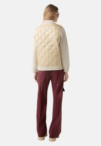 Beżowa pikowana kamizelka puchowa z białymi rękawami, elastycznym dołem, w połączeniu z bordowymi spodniami o szerokich nogawkach. Charakteryzuje się gładką fakturą i minimalistycznym designem.