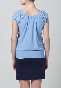 Blusa de color azul claro con mangas fruncidas y dobladillo inferior elástico y fruncido. Combinada con una falda ceñida de color azul marino, de tela suave.