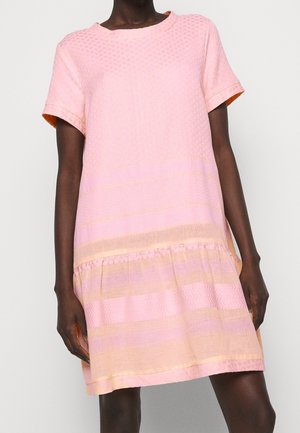 Dunkelhäutige Person, die ein locker sitzendes, ärmelloses Kleid in Kniehöhe mit rosa und pfirsichfarbenen, strukturierten horizontalen Streifen trägt.