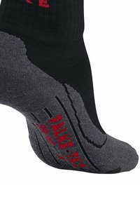 Chaussette noire et grise avec une partie supérieure côtelée, semelle grise rembourrée, texte "FALKE" en rouge et détails texturés au bas pour l'adhérence.