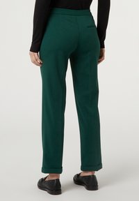 Pantalon vert à jambes droites en matière lisse, avec une poche arrière et des revers retroussés, associé à des chaussures noires.