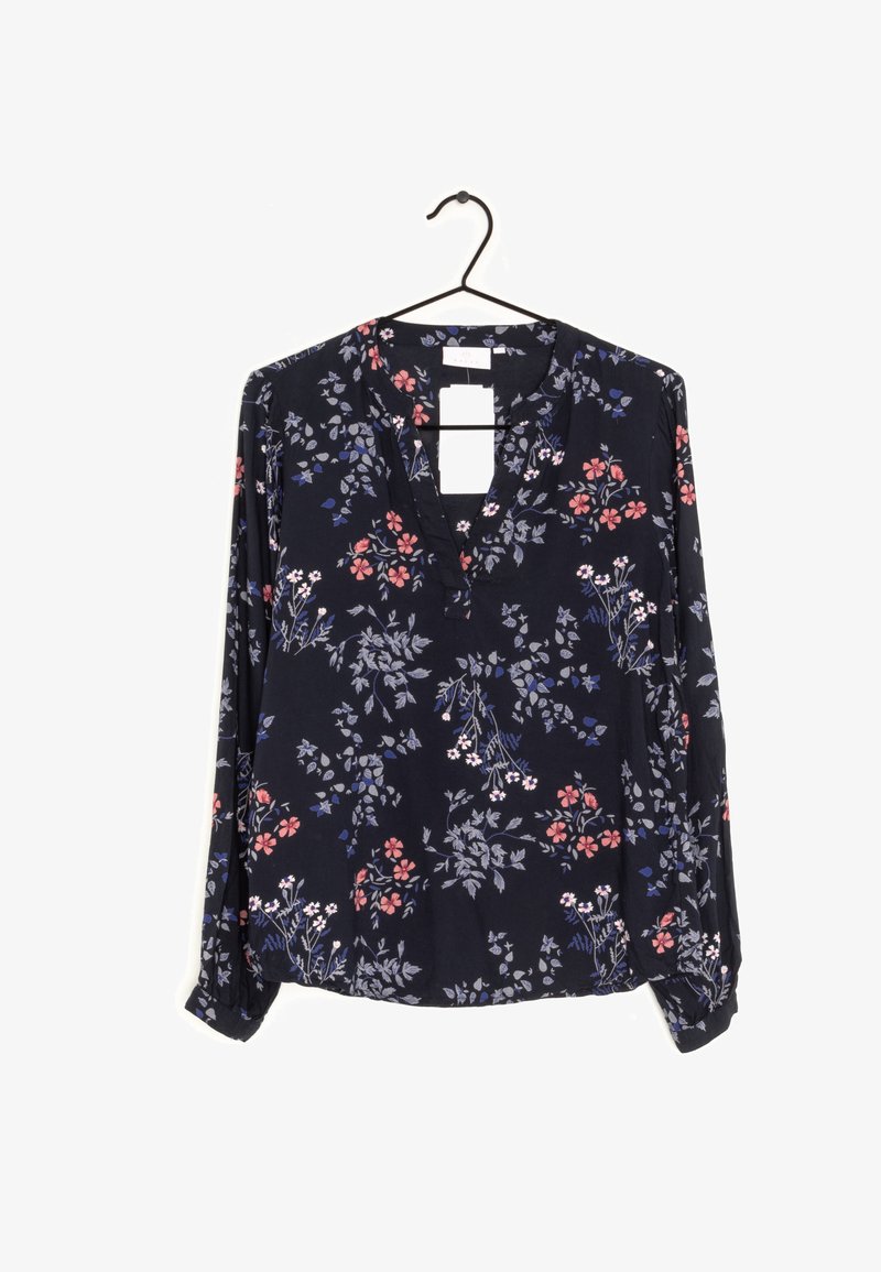 Blouse bleu marine à manches longues avec un motif floral rose et lavande, col en V, suspendue sur un cintre noir sur fond blanc.