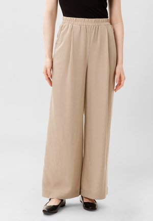 Béžové široké kalhoty s plisovaným designem a elastickým pasem, vyrobené z lehké látky. Mají uvolněný střih a minimální zdobení.