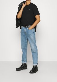 Camiseta negra, jeans de mezclilla azul claro con los puños enrollados, botines negros y una chaqueta de cuero negra colgada sobre el hombro.