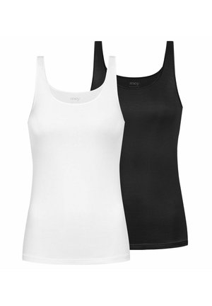 Frau mit geflochtenem Haar, die ein weißes Tanktop und weiße Unterwäsche trägt, steht vor einem schlichten hellen Hintergrund.