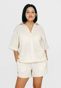 Beige Kurzarmhemd mit Knopfleiste und Kragen, kombiniert mit passenden Shorts. Beide Teile bestehen aus einem weichen, leichten Stoff.