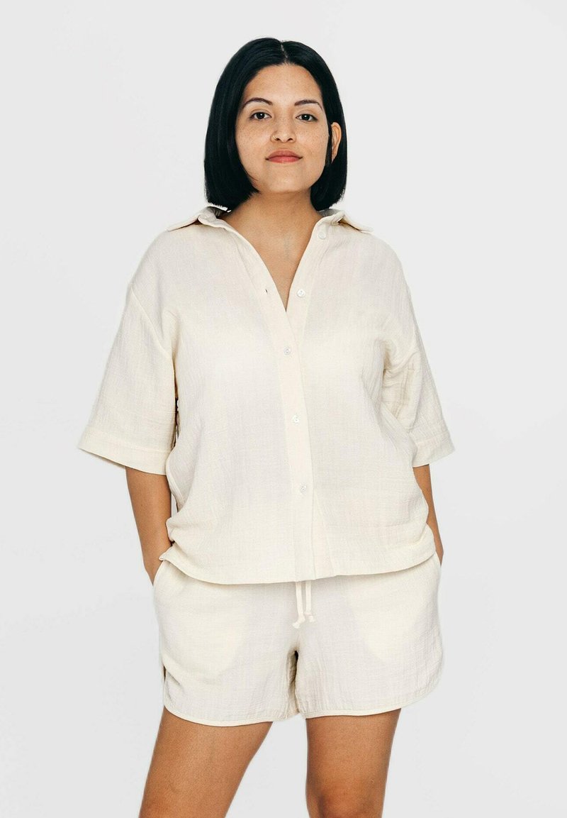 Beige Kurzarmhemd mit Knopfleiste und Kragen, kombiniert mit passenden Shorts. Beide Teile bestehen aus einem weichen, leichten Stoff.