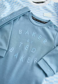 Svetlomodrá mikina s textúrovaným logom "BAKER by TED BAKER." Má zaoblený výstrih, mäkkú bavlnenú tkaninu a gombíkové ozdoby na ramene.