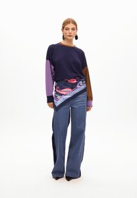 Granatowy sweter z kolorowymi rękawami w fioletowym i brązowym kolorze, w połączeniu z szerokimi dżinsami. Posiada akcent w postaci wzorzystego szalika w talii.