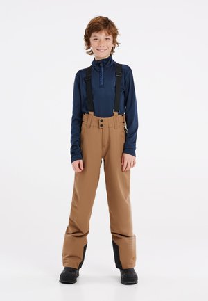 Pantaloni da neve marroni con bretelle nere regolabili, due bottoni frontali e dettagli neri alle caviglie. Sotto una maglia a maniche lunghe blu navy.