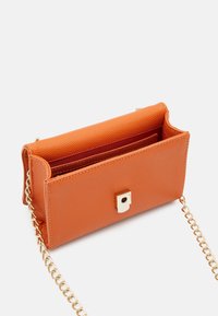 Orange fusk läder crossbody-väska med en texturerad yta, guldkedjestrap och ett fyrkantigt magnetlås. Inuti finns en röd foder.