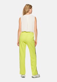 Lightweight, sleeveless white top with a back pleat paired with bright neon green sweatpants featuring side stripes and elastic waistband.