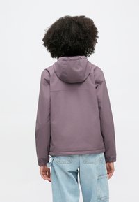 Lila huva med elastiska muddar och justerbar fåll, gjord av lätt material, matchad med ljusblå cargobyxor.