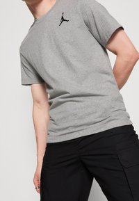 Camiseta gris de algodón con un logo Jumpman negro en el pecho izquierdo, combinada con pantalones cargo negros para un look casual.