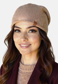 Strikket beige hue med en rullet kant, der har et lædermærke på siden. Blød tekstur og en afslappet pasform.