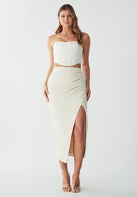Completo bianco a due pezzi con top aderente senza spalline caratterizzato da cuciture verticali e gonna lunga con spacco alto e dettagli arricciati.