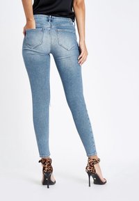 Jeans ajustados de mezclilla azul clara con una textura suave, cintura alta y dos bolsillos traseros. Combinados con sandalias negras de tacón alto con un acento de estampado de leopardo.