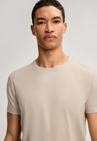 Beige kortærmet T-shirt lavet af blødt stof. Har en rund halsudskæring og en diskret broderet "JOOP!" logo på brystet. Glat tekstur.