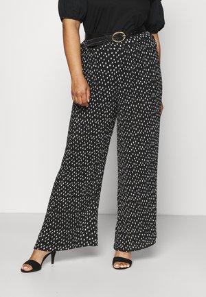 Pantalons larges noirs à pois blancs, avec un tissu texturé et une taille ceinturée. Assortis à des talons ouverts noirs.