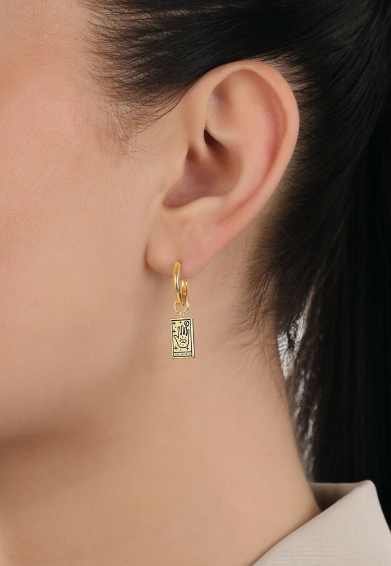 Guldörhänge med en rektangulär charm som har ett tryckt handmönster och texten "VÄRLDEN" längst ner.