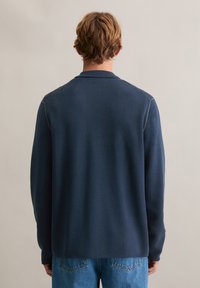 Granatowa koszula z długim rękawem i kołnierzykiem polo, z kontrastowymi przeszyciami. Tkanina wydaje się gładka z wyraźną fakturą.