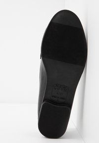 Semelle d'une chaussure formelle noire montrant les motifs de la semelle et les détails de taille "New Look 4 37 Made in China" sur fond blanc.