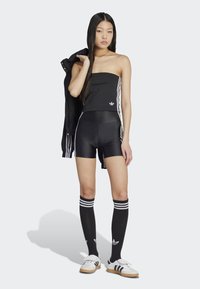 Čierny top bez ramienok s bielym logom, čierne nohavice s vysokým pásom, čierne ponožky po kolená s bielymi pruhmi a biele tenisky s čiernymi akcentmi.