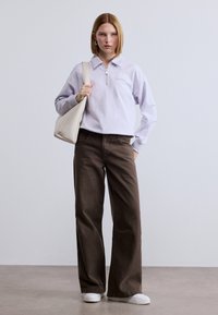 Ανοιχτό μωβ φούτερ με φερμουάρ, καφέ παντελόνια με φαρδιά μπατζάκια, λευκά αθλητικά παπούτσια και κρεμ τσάντα χειρός. Λείο ύφασμα με ελάχιστες λεπτομέρειες από μάρκα.