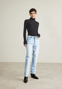 Maglione nero a coste con collo alto e maniche lunghe, abbinato a jeans dritti azzurri e stivaletti neri con punta a punta e tacco.