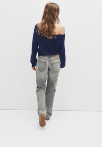 Pull marine à col bateau associé à un jean gris clair à jambes droites, avec un écusson en cuir à l'arrière et une finition texturée.