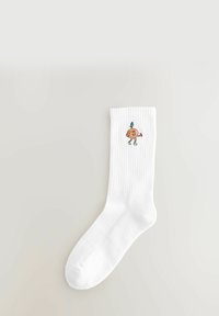 Hvid, ribbet crew-sok med en lille broderet orange figur, der bærer grønne sko og et grønne blad på toppen.