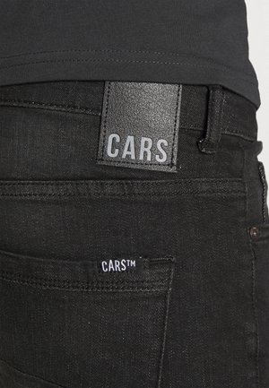 Zwarte denim jeans met een leren merklabel met daarop "CARS" boven de achterzak en een klein stoffen label met de tekst "CARS™".