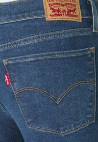 Mörkblå denimjeans med orange sömmar, en synlig bakficka med en sydd design och en brun läderetikett med varumärkesdetaljer.