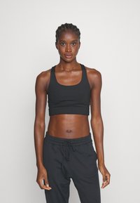 Svart atletisk crop top med rund hals og brede stropper, sammen med svarte joggebukser med elastisk liv og snor.