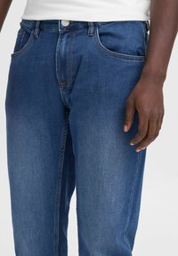 Jeans de mezclilla azul oscuro con un corte recto, que cuentan con bolsillos frontales, presillas para cinturón y detalles de costura sutiles, exhibidos sobre un fondo neutro.