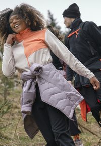 Chaqueta de forro polar con bloque de color naranja y crema, cierre de cremallera y textura suave. Capa acolchada lavanda anudada a la cintura.