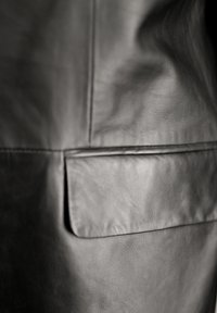 Czarna skórzana kurtka z widocznym detalem kieszeni, gładką teksturą i subtelnym wzorem na materiale, z czystymi, minimalistycznymi liniami.