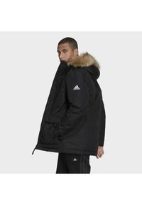 Černá zateplená parka s kapucí z kožešiny, zapínání na zip, dvě přední kapsy a logo Adidas na rukávu.