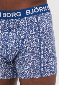 Boxers en coton avec un motif floral bleu sur un fond blanc, comportant une ceinture bleue avec le texte « BJÖRN BORG », et des surpiqûres bleues contrastantes.