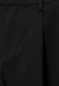 Pantalon noir sur mesure en tissu lisse. Il présente un devant plat avec des détails de couture subtils et des poches latérales.