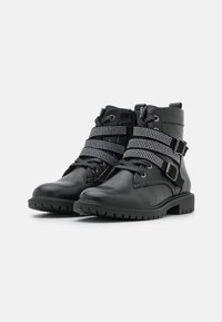 Botas negras de piel hasta el tobillo que presentan dos cintas decorativas con pedrería, puntera redondeada, suela texturada y cierre frontal con cordones.